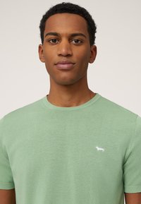 Lichtgroen T-shirt met korte mouwen, gemaakt van zachte stof, met een ronde hals en een klein wit teckel-logo op de linkerkant van de borst.