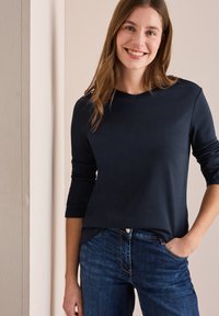 Mörkblå långärmad skjorta med rund halsringning, mjuk textur och avslappnad passform, kombinerad med mörka denimbyxor med fickor och sömdetaljer.