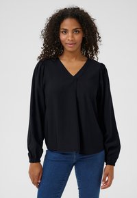 Blouse noire à col en V, avec des manches longues froncées et un détail plissé à l'avant. Le tissu a une texture lisse.