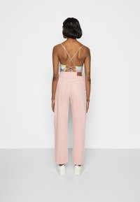 Calças de cintura alta rosa com pernas largas, combinadas com uma blusa de costas cruzadas com padrão floral. A modelo usa sapatilhas brancas.