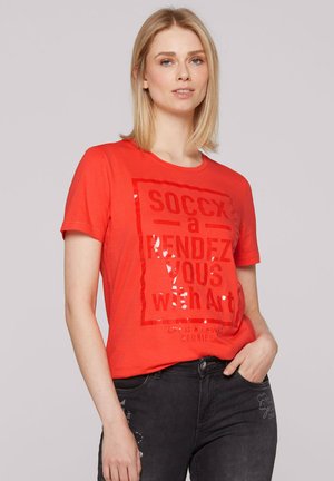 T-shirt rouge à manches courtes avec un texte imprimé brillant disant "SOCCX un RENDEZ-VOUS avec l'Art." Tissu en coton doux, coupe décontractée.