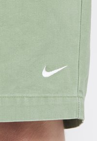Shorts vert clair en tissu texturé avec un logo Nike blanc brodé sur l'ourlet inférieur. Design simple sans motifs supplémentaires.