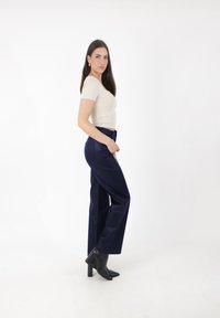 Beżowa dopasowana koszulka, wysokie granatowe szerokie spodnie, gładki materiał, boczne kieszenie, czarne skórzane botki na kostkę z blokowym obcasem.