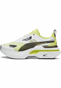 Sneaker giallo e bianco con parte superiore in rete testurizzata, dettagli neri e verdi, suola bianca spessa e collare imbottito per il supporto.