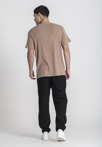 Hnedé rebrované tričko s krátkymi rukávmi, skombinované s čiernymi nohavicami a bielymi teniskami. Tkanina vyzerá textúrne a neformálne.