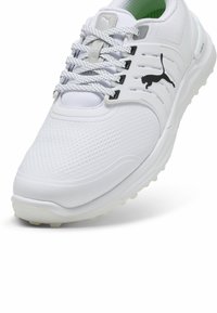 Vit golfskor gjorda av strukturerad mesh och syntetiska material. Utrustad med gummisula med utstickande delar, snörningssystem och en Puma-logotyp.