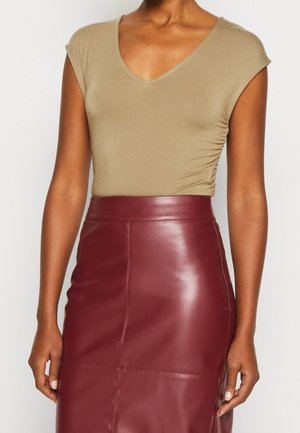 Olivi vihreä tiukka paita lyhyillä hihoilla ja V-pääntiellä, yhdistettynä vartaloa myötäilevään burgundinpunaiseseen nahkahameeseen, joka korostaa sileää tekstuuria.