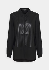 Blouse noire avec un panneau avant brillant semblable à du cuir et des manches en tissu mat. Dispose d'un col classique et d'une fermeture à boutons, manches longues.