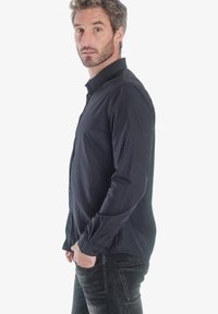 Camisa de manga larga azul marino hecha de tela suave con un cuello abotonado, que presenta un corte ajustado y detalles de costura sutiles.