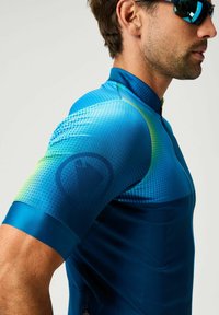 Maillot de cyclisme bleu en matériau léger et extensible. Doté d'un motif à pois, d'une fermeture éclair et de manches courtes avec une finition lisse.