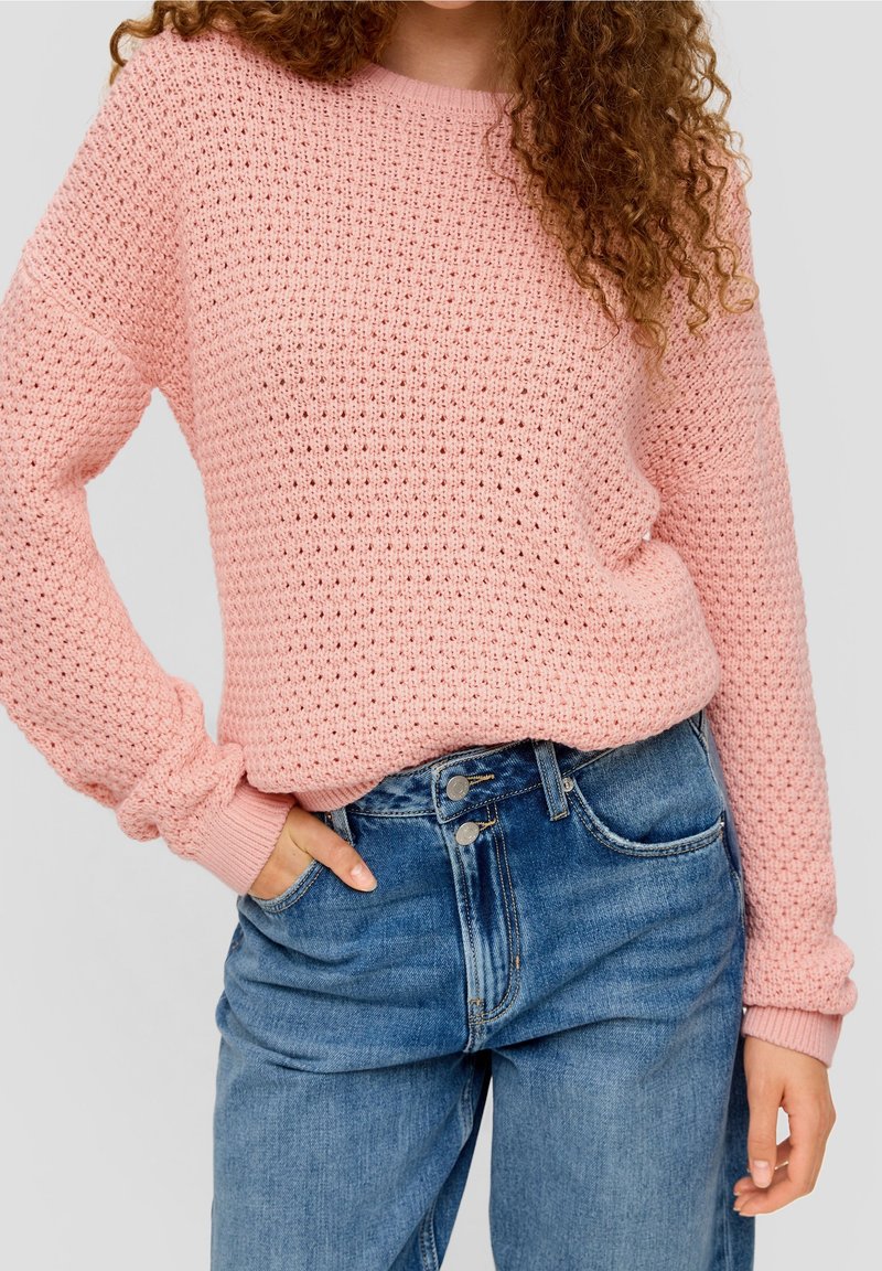 Pull en tricot rose avec un motif texturé, des poignets côtelés et un col rond, associé à un jeans taille haute bleu clair.