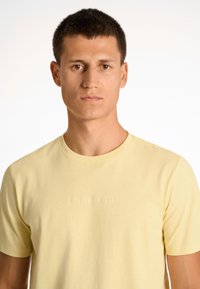 T-shirt giallo a maniche corte realizzata in morbido cotone, con scollatura rotonda e nome del marchio "LINDBERGH" in rilievo sul petto.