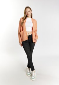 Őszibarack színű, nyitott elejű kardigán, két zsebbel, fehér crop top-pal és fekete, slim-fit farmernadrággal párosítva. Fehér és pasztell színű sportcipők.