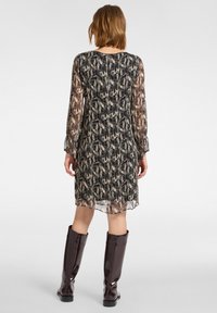 Bedrucktes, transparentes Kleid in Beige-, Schwarz- und Brauntönen mit langen, durchsichtigen Ärmeln und lockerer Passform. Kombiniert mit knielangen braunen Stiefeln.