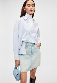 Ανοιχτό μπλε πουκάμισο με ρίγες και γιακά, συνδυασμένο με ανοιχτό τζιν φούστα. Κρατά μια μικρή μπλε τσάντα χειρός· φοράει μαύρες μπότες μέχρι το γόνατο.