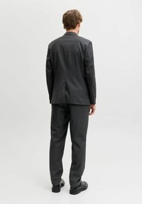 Garnitur w ciemnoszarym kolorze w drobną prężkę, o kroju dopasowanym. Marynarka z kołnierzem z wycięciem i pojedynczym rozcięciem z tyłu. Spodnie o prostych nogawkach.