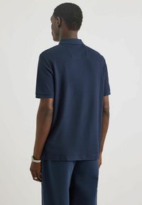 Marineblaue Poloshirt mit kurzen Ärmeln, aus atmungsaktivem Stoff, mit weicher Textur und klassischem Kragen. Maßgeschneiderter Schnitt mit minimalen Details.