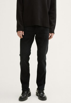 Black denim jeans feature a slim fit with a smooth texture. Paired with black lace-up shoes and a dark knit sweater.