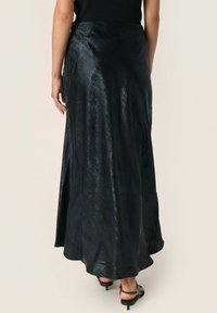 Sort satin maxi nederdel med en glat tekstur, flydende form og sideslids. Har en tætsiddende talje og en subtil glans. Justerbare stropper er synlige.