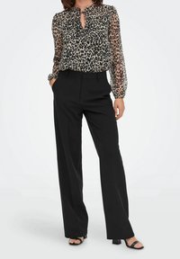 Blusa trasparente con stampa leopardata, con scollo a chiave e dettagli arricciati, abbinata a pantaloni neri a vita alta e sandali neri con tacco.