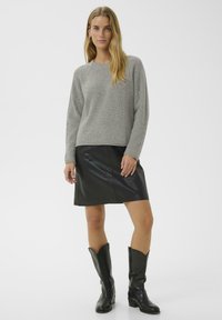 Pull gris à côtes avec des manches longues, associé à une mini-jupe en cuir noir et des bottes noires jusqu'aux genoux, sur fond blanc.