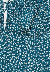 Top de tela color teal con un patrón floral blanco texturizado, que presenta un escote recogido y detalles de lazo. Material ligero con caída suave.