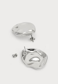 Boucles d'oreilles en argent avec une forme abstraite et organique ; surface polie avec une texture lisse, comprenant un tige et une protection pour un port sécurisé.
