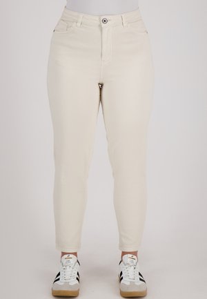 Crème gekromde jeans hebben een hoge taille, vijf zakken en een sluiting met een voorste knoop. In combinatie met witte sneakers met zwarte strepen.