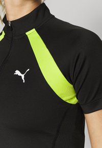 Černý sportovní top s vysokým límečkem, krátkými rukávy a jasně limetkovými akcenty s bílým logem Puma na hrudi.