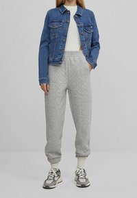 Džínová bunda, šedé prošívané joggery, bílé svetr a šedé tenisky s černými a bílými akcenty. Volný střih, žebrované manžety a pas.