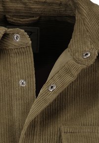 Olivengrünes Cordhemd mit geripelter Textur, ausgestattet mit silbernen Druckknöpfen und einer Brusttasche. Das kragenlose Design betont die Struktur.