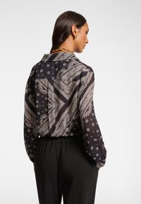 Blusa de patrón negro y blanco con mangas largas y cuello clásico, que presenta diseños de paisley y florales. Tejido suave, corte amplio.