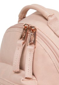 Ljusrosa ryggsäck med dubbla guldfärgad dragkedjor, mjuk mockaliknande textur och hållbara canvashandtag. Detaljerad sömnad längs sömmarna.
