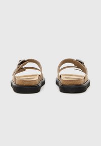 Sandales marron avec deux brides réglables, une semelle texturée et une semelle en caoutchouc noir, avec un détail de boucle métallique.