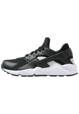 Czarno-biały sportowy sneaker z siateczkową i skórzaną cholewką, grubą teksturowaną białą podeszwą oraz czarną plastikową klatką na piętę na białym tle.