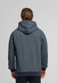 Kapuzensweatshirt aus dunkelblauem Textil mit strukturiertem Stoff, gemustertem Webmuster, gerippten Bündchen und abgerundetem Saum. Die Rückansicht zeigt die Kapuze und die Nähte.
