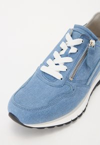 Baskets bleu clair avec lacets blancs, fermeture éclair latérale, semelle intermédiaire blanche et semelle extérieure noire, montrant les détails de l'avant et du côté extérieur.