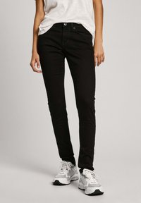 Svarta smala jeans med en klassisk femficksdesign, tillverkade av denimtyg med en slät yta, matchade med vita sneakers.