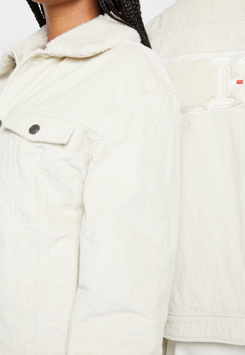 Femme portant une veste en velours côtelé crème avec col en shearling et boutons-pression, montrant les détails avant et arrière, y compris le logo de marque embossé.