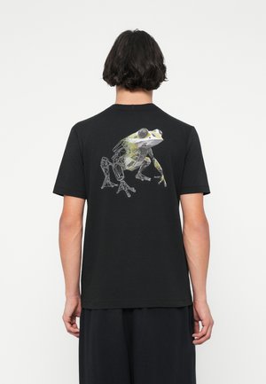 Sort bomulds t-shirt med et grafisk design af en grøn frø med geometriske konturer på ryggen. Korte ærmer og rund hals.