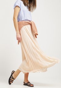 Skládaná světle broskvová sukně s volným designem, spárovaná s krátkým rukávem světle modré blůzce a pleteným růžovým svetr, který je uvázaný v pase.