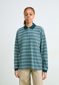 Polo a maniche lunghe in teal con righe orizzontali, dotato di colletto e un piccolo logo sul petto. Abbinato a pantaloni beige.