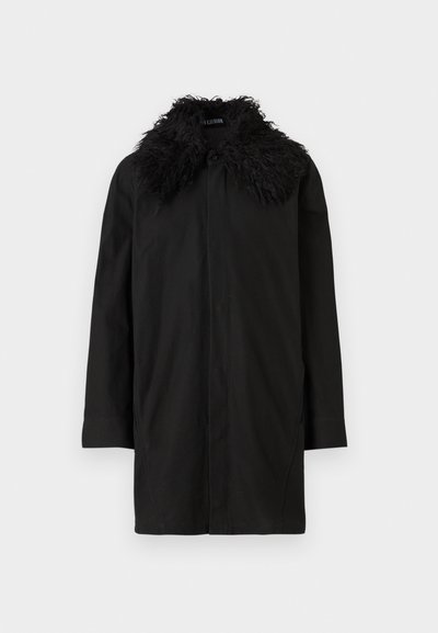 Casaco preto de comprimento médio com mangas longas e um grande colar de pele texturizada, apresentado contra um fundo branco.