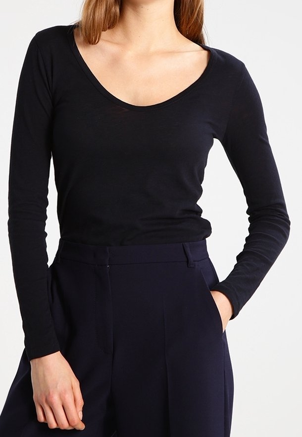 Top nero a maniche lunghe con scollatura a barca, realizzato in tessuto morbido e leggero; indossato con pantaloni scuri sartoriali.