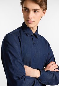 Camicia button-up blu navy realizzata in denim, caratterizzata da un colletto strutturato, maniche lunghe, logo del marchio discreto e dettagli dei bottoni a contrasto.