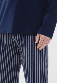 Camisa de manga larga marina combinada con pantalones de pijama a rayas en navy y blanco. El tejido parece de algodón, con una textura suave y un ajuste relajado.