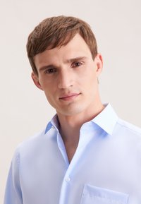 Camicia azzurro chiaro con bottoni e taschino, con colletto e una fodera interna a motivo discreto. Tessuto liscio con una finitura lucida.