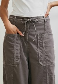 Grijze cargo-broek met brede pijpen en een trekkoord in de taille, voorzien van grote zijzakken en een gestructureerde stof. Effen top, minimale hardware details.
