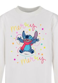 Witte langemouwen shirt met een cartoon blauwe figuur met een rode sjaal, omringd door kleurrijke stippen en de woorden "merry" in roze en groen.