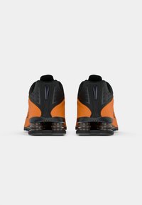 Tênis atléticos pretos e laranjas com acabamento texturizado, apresentando amortecimento visível na sola e detalhes perfurados na parte superior.